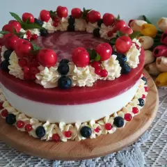 Wykwintny tort z warstwą białego kremu i błyszczącą, czerwona żelką truskawkową, ozdobiony bitą śmietaną, owocami i listkami mięty.