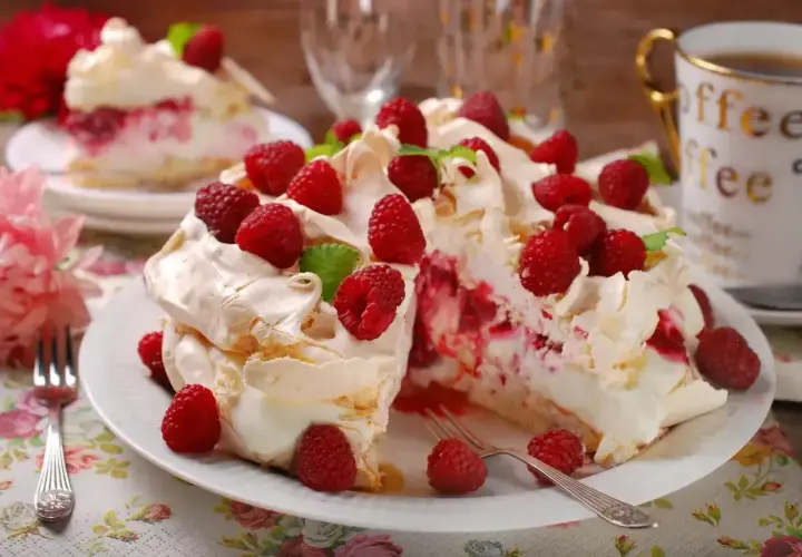 Pyszny tort bezowy z mascarpone i malinami, udekorowany świeżymi owocami i listkami mięty. Idealny na deser.