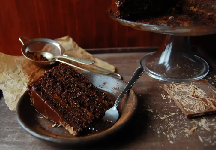 Wilgotny tort czekoladowy z kremem nutella, posypany kakao, czeka na widelca. Obok kawałek czekolady.