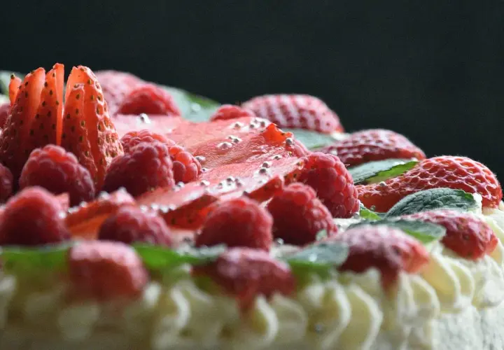 Pyszny tort dobosza, udekorowany malinami, truskawkami i listkami mięty, posypany srebrnymi kuleczkami.