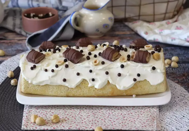 Puszysty biszkopt z kremem, udekorowany kawałkami batoników Kinder Bueno White, orzechami i czekoladowymi kuleczkami.
