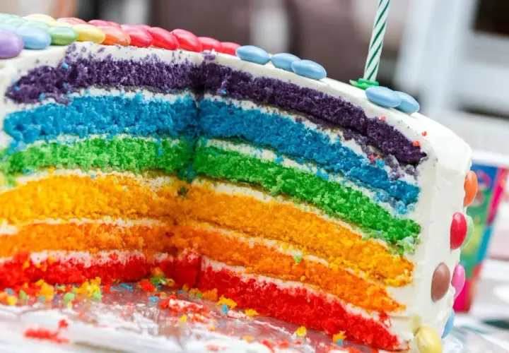 Kolorowy tort tęczowy z warstwami ciasta w odcieniach czerwieni, pomarańczu, żółci, zieleni, błękitu i fioletu, ozdobiony cukierkami.