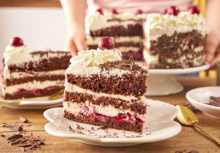 Pyszny tort szwarcwaldzki z mascarpone, przełożony kremem i wiśniami, ozdobiony czekoladowymi wiórkami i wisienką.